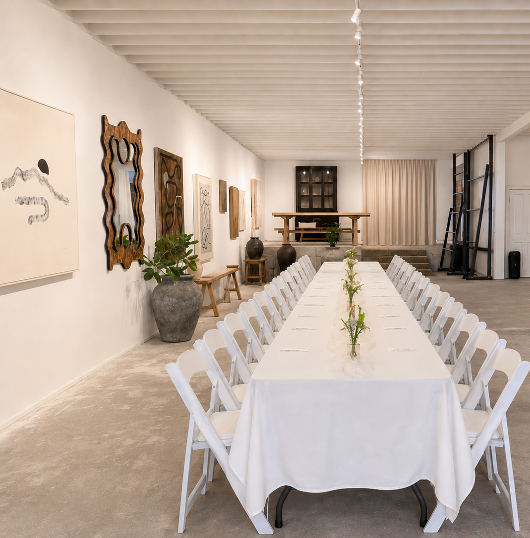 Long table with white tablecloth and chairs in a modern room with artwork and plants.